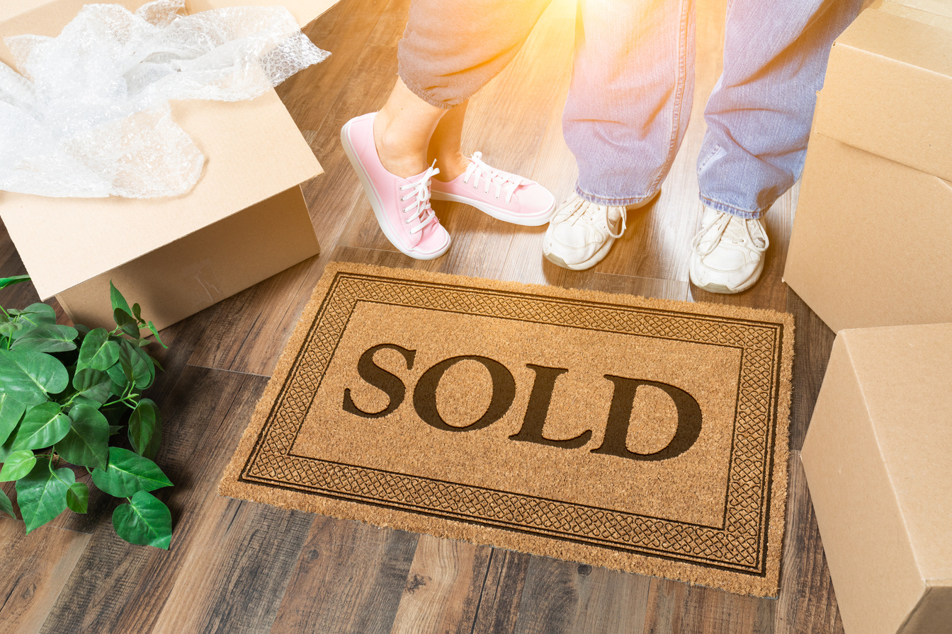 Man and Woman Standing near Sold Welcome Mat, Moving Boxes and P
